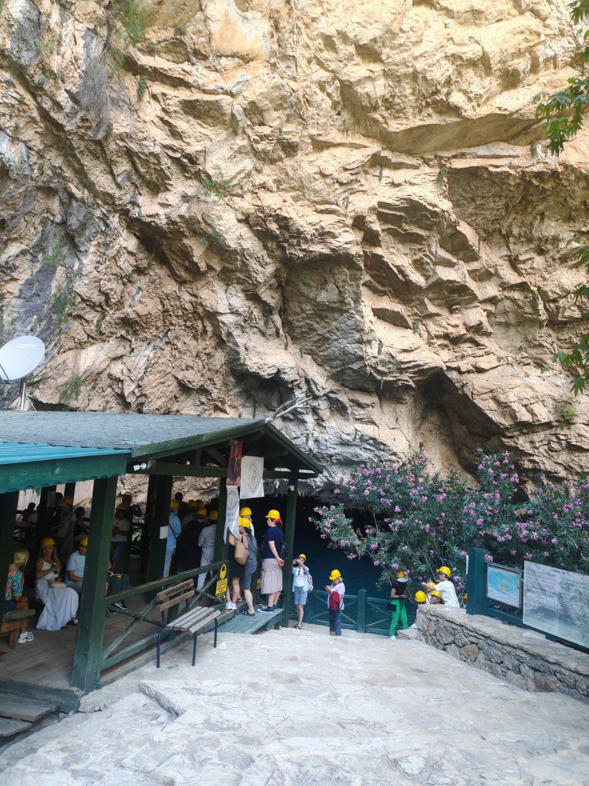 Mağara girişindeki ahşap gölgelikte sarı bareti takmış ziyaretçiler sırada bekliyor