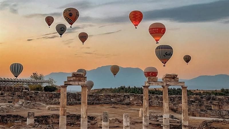 Antik sütun kalıntılarının üzerinde gün doğumunda çok sayıda renkli sıcak hava balonu süzülüyor