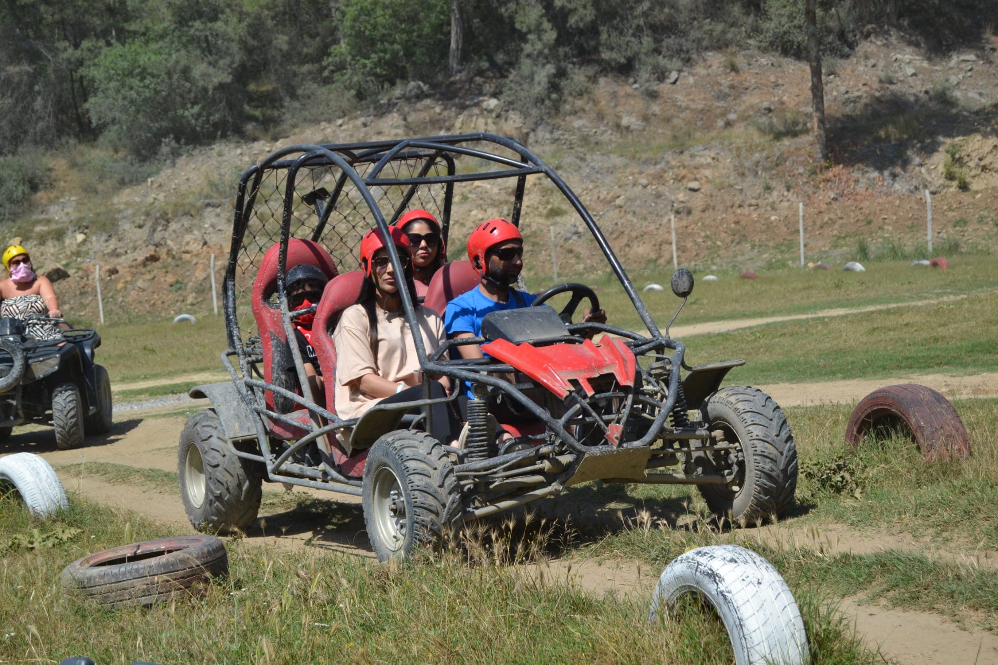 Dört kişilik kırmızı koltuklu buggy lastiklerle çevrili çim parkurda ilerliyor, arkada tepeler