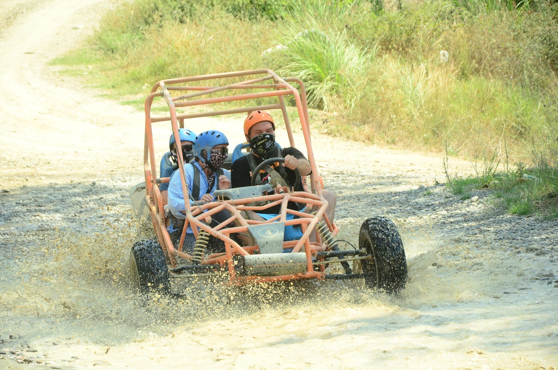 Üç kişilik buggy ekibi kasklarıyla toprak yolda su sıçratarak ilerliyor