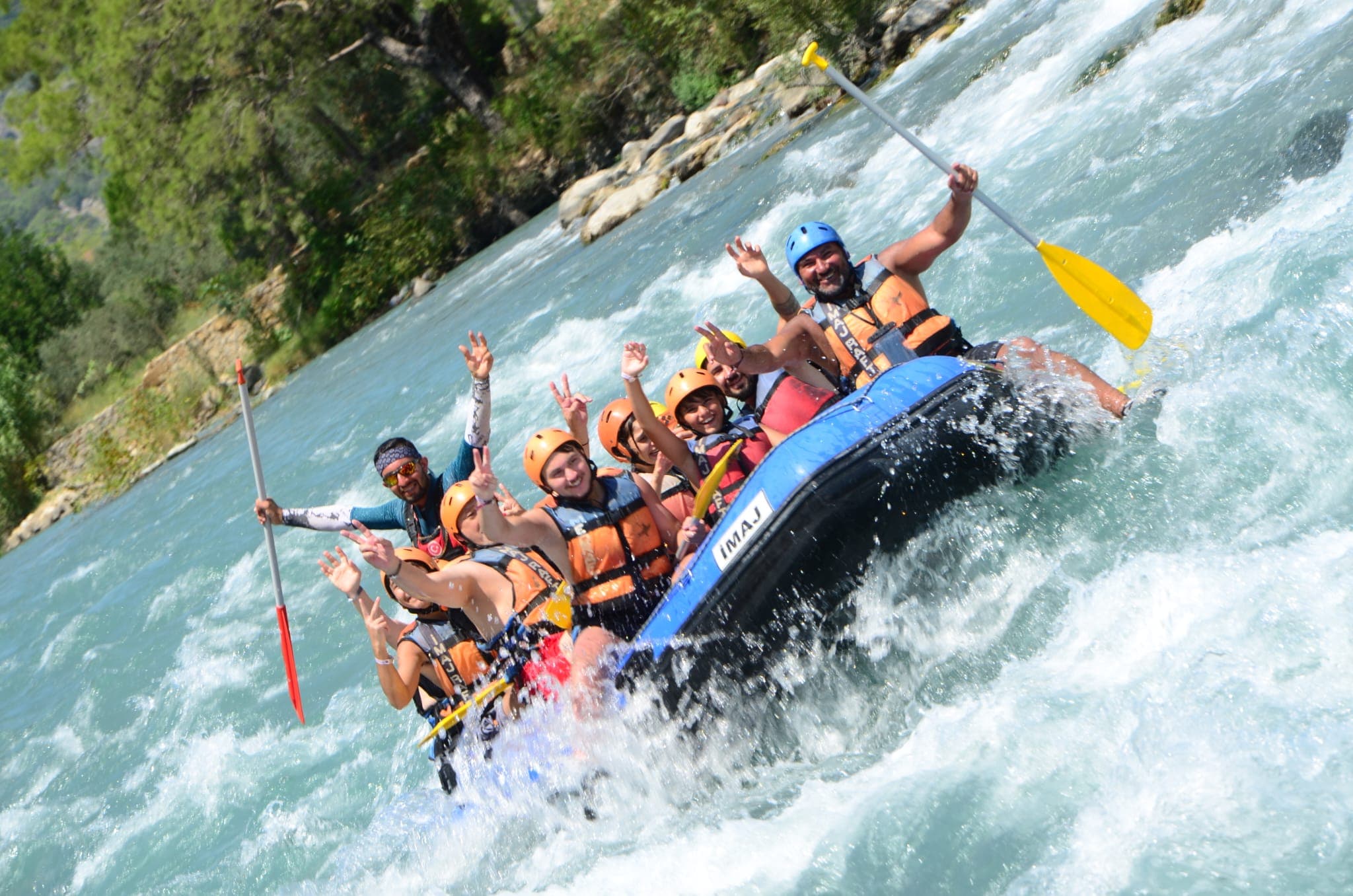 Rafting botu köpüklü akıntıda ilerlerken katılımcılar kürekleriyle selam veriyor