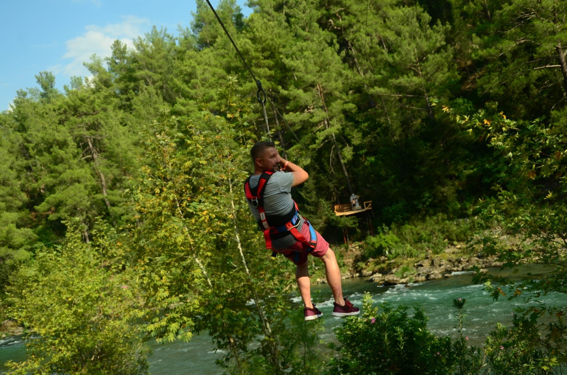 Bir katılımcı emniyet kablosuna bağlı halde nehir üzerinde zipline'da ilerliyor