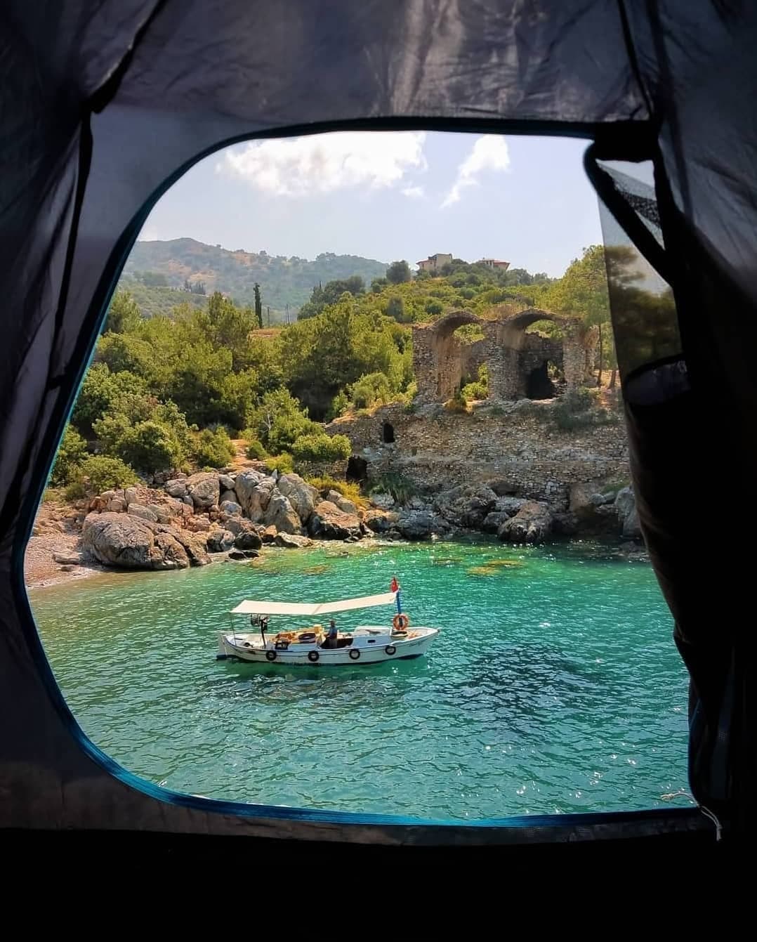 Kıyıdaki antik taş kemer kalıntılarının önünde küçük beyaz bir tekne turkuaz koyda demirlemiş