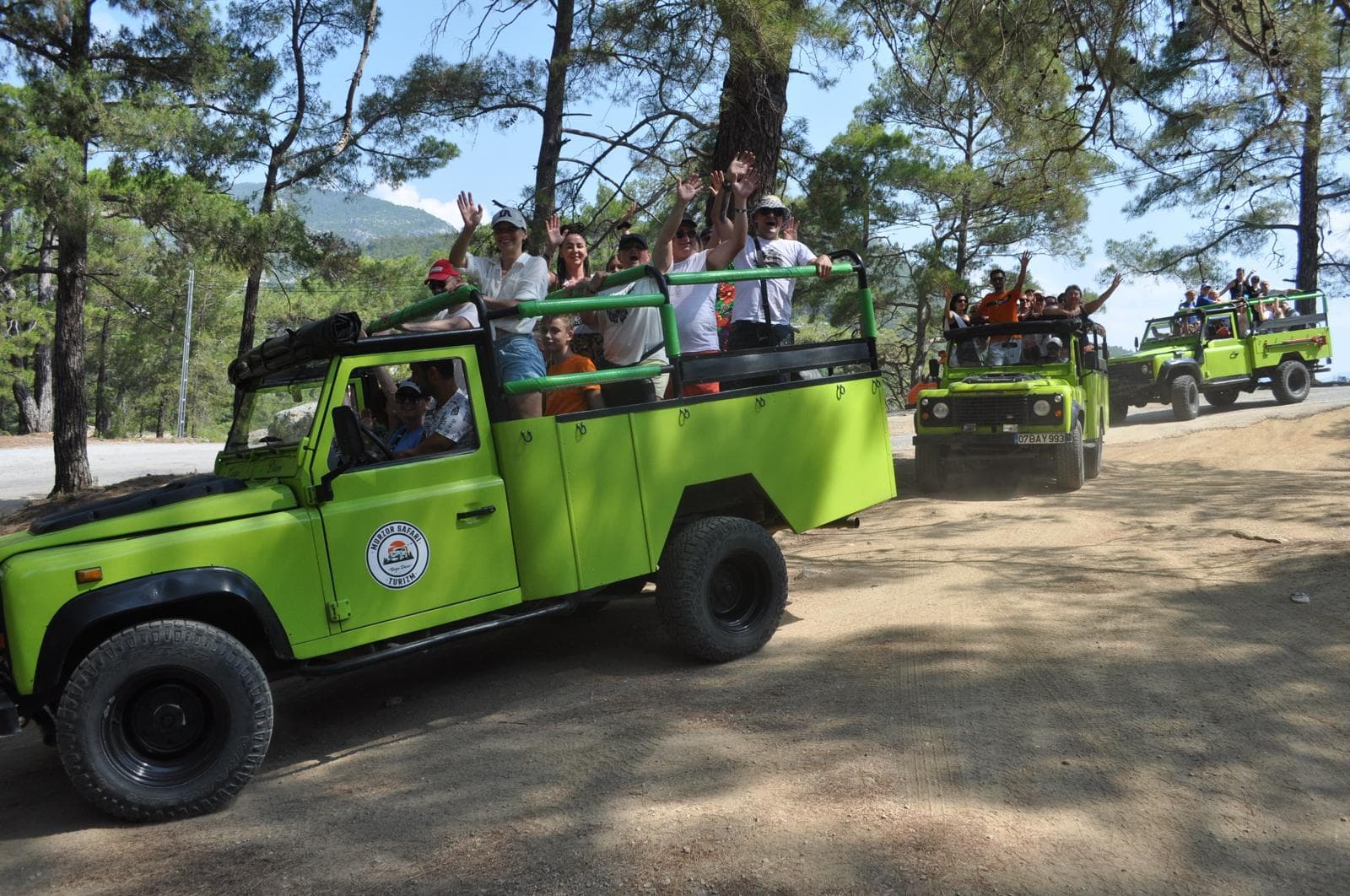 Yeşil açık üstü jeep'ler ormanlık toprak yolda konvoy halinde ilerliyor