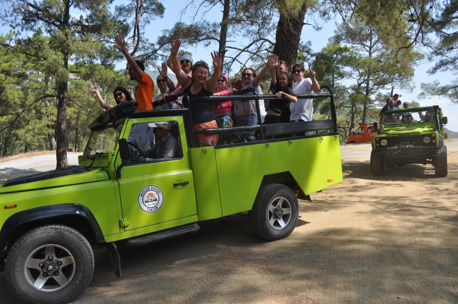 Misafirler açık üstü jeep'in içinde ve üzerinde otururken araç toprak yolda duruyor