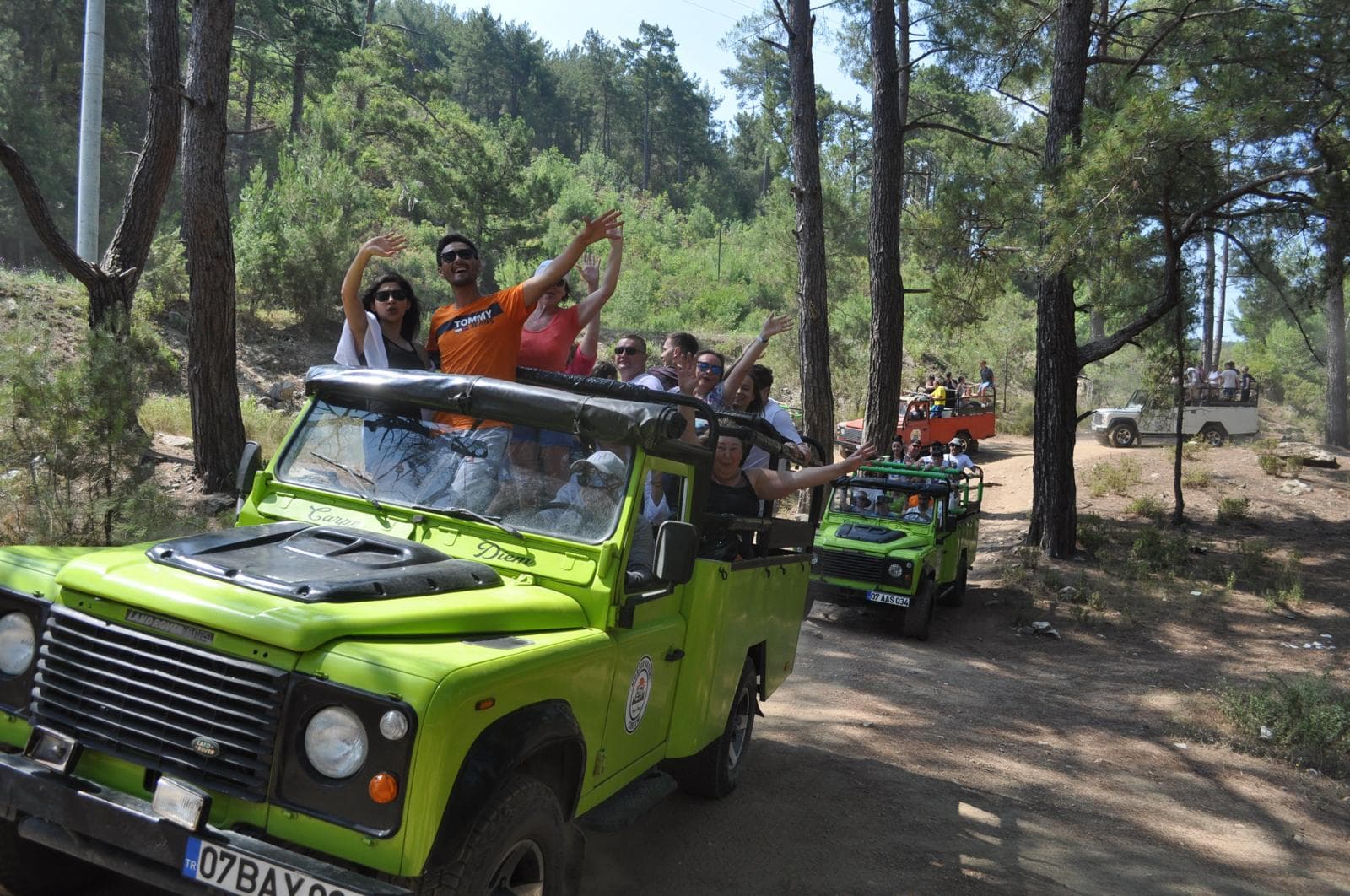 Yeşil jeep konvoyu toz kaldırarak toprak ormanlık yolda ilerliyor