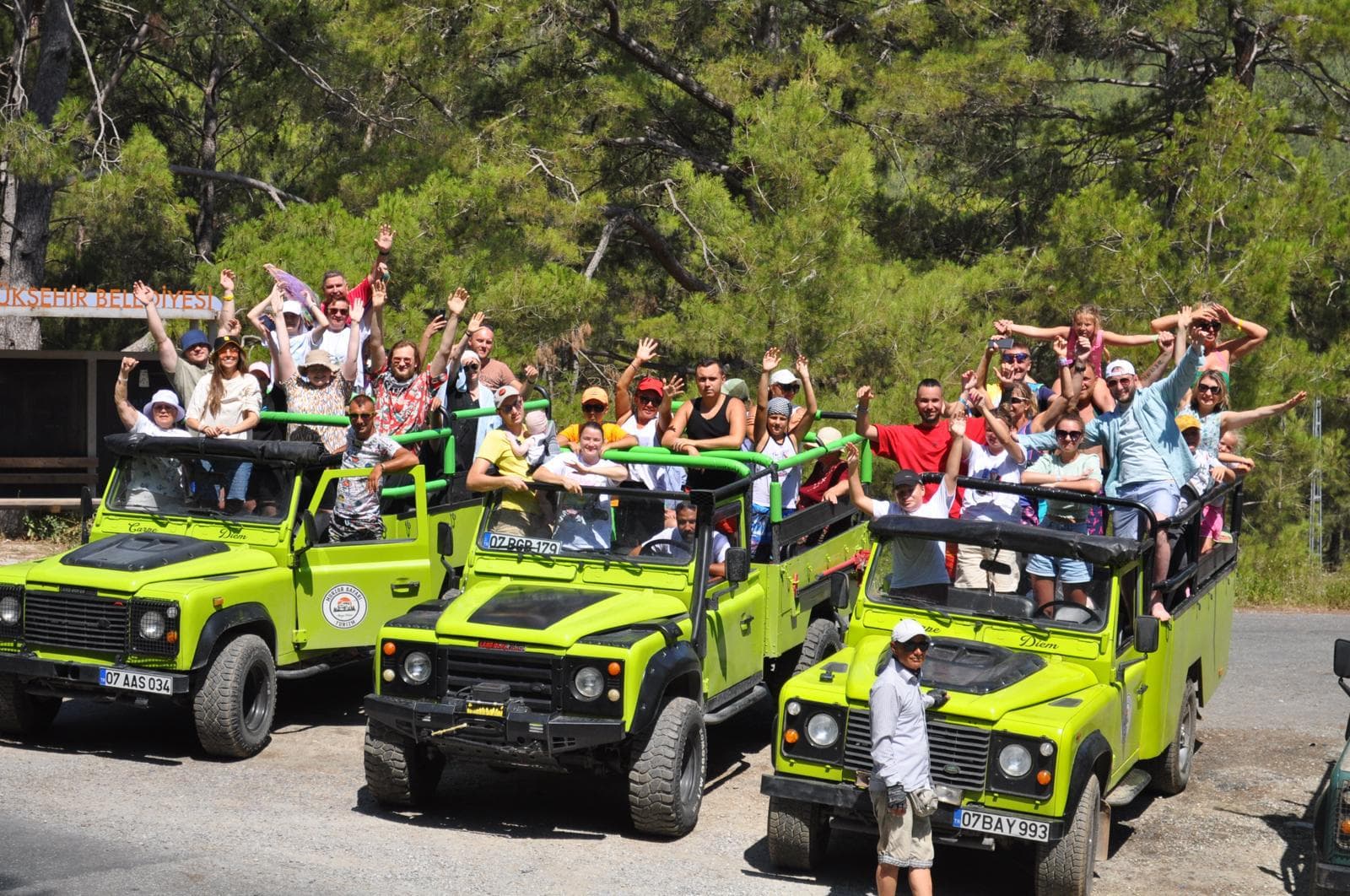 Misafirler jeep'in üzerinde ayakta durup güzergâhı izliyor, araç ormanlık yolda duruyor