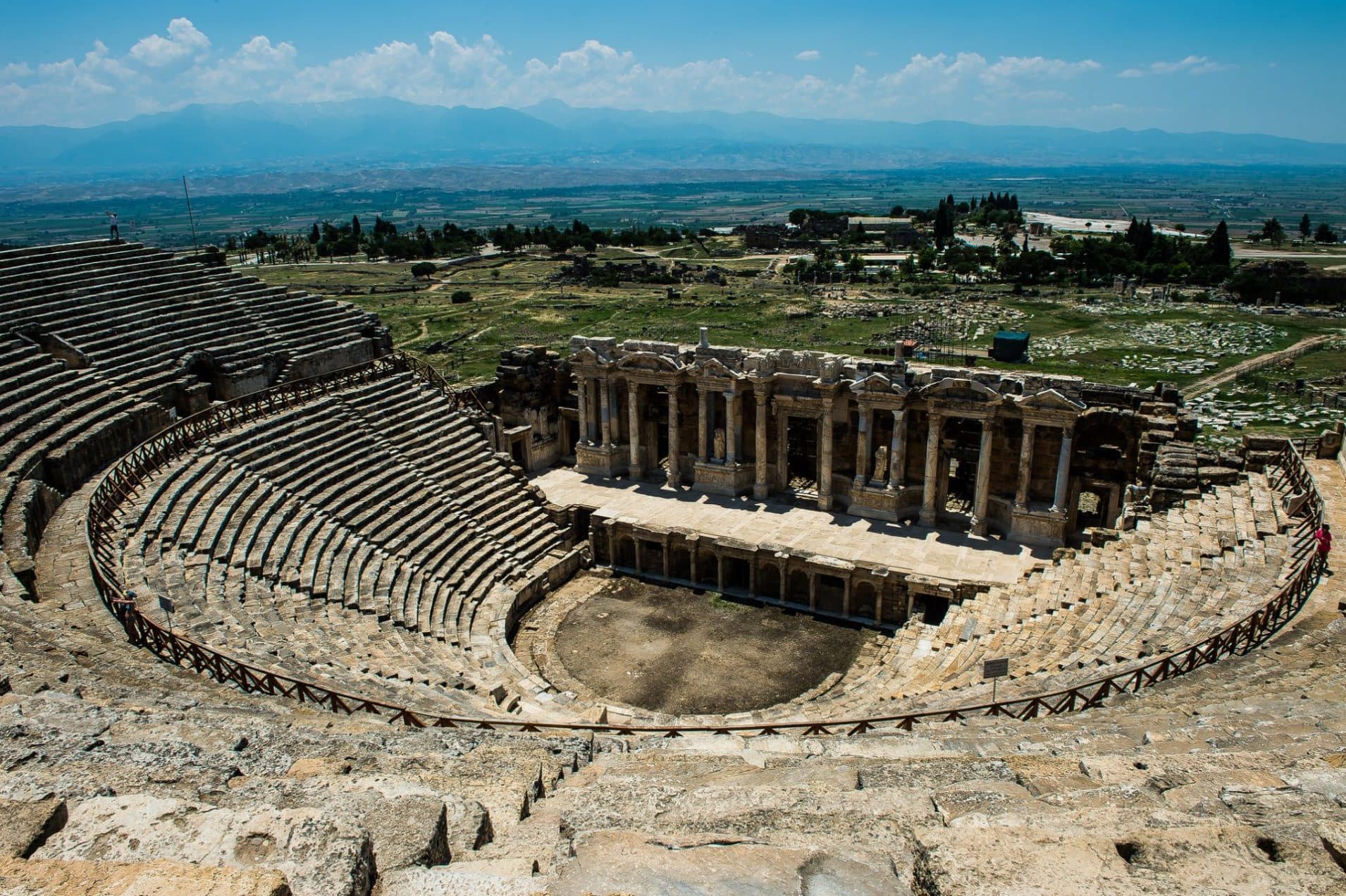Hierapolis Antik Tiyatrosu'nun kuşbakışı görünümü, taş sıralar ve sahne binasının mermer sütunları, arkada geniş bir ova uzanıyor