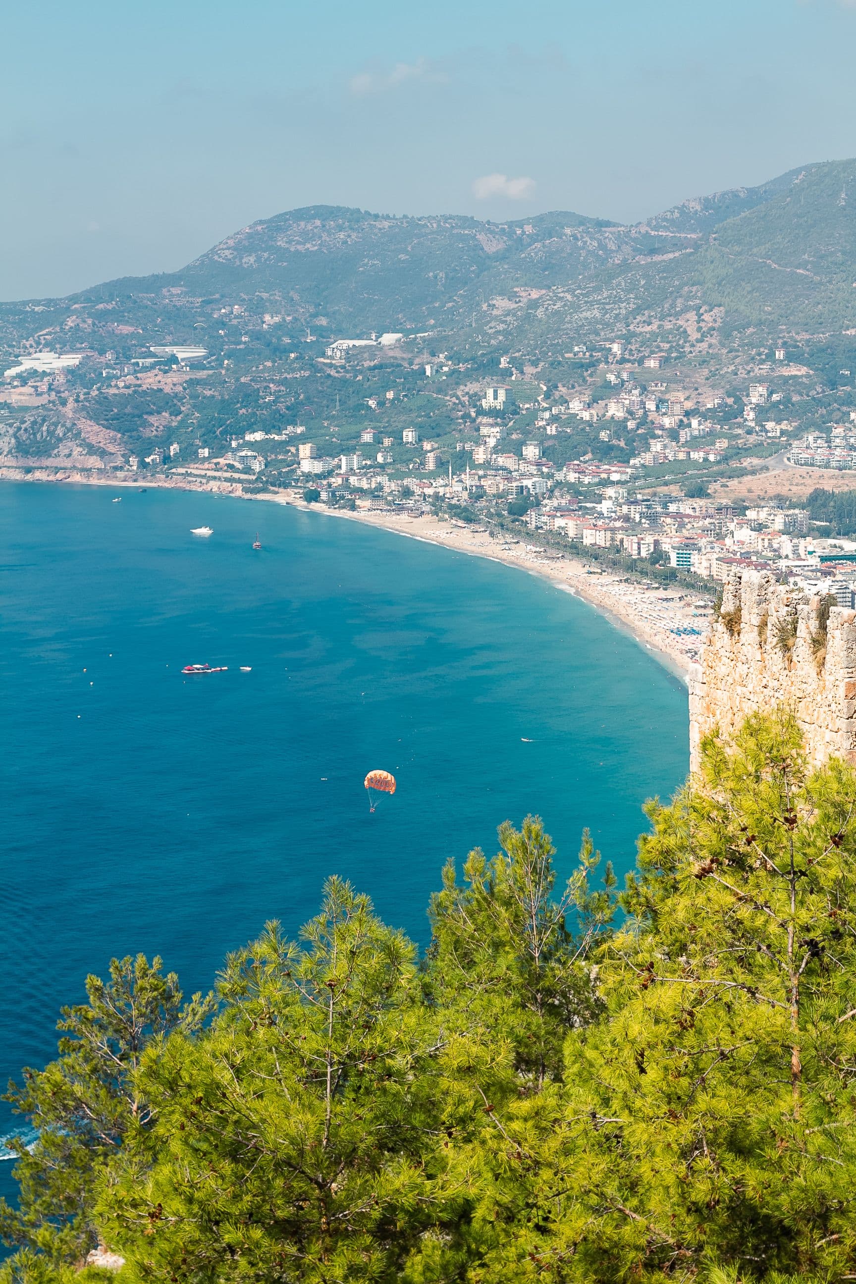 Alanya Kalesi'nin sur duvarlarından Kleopatra Plajı'na bakan manzara, denizin üzerinde renkli bir paraşüt süzülüyor