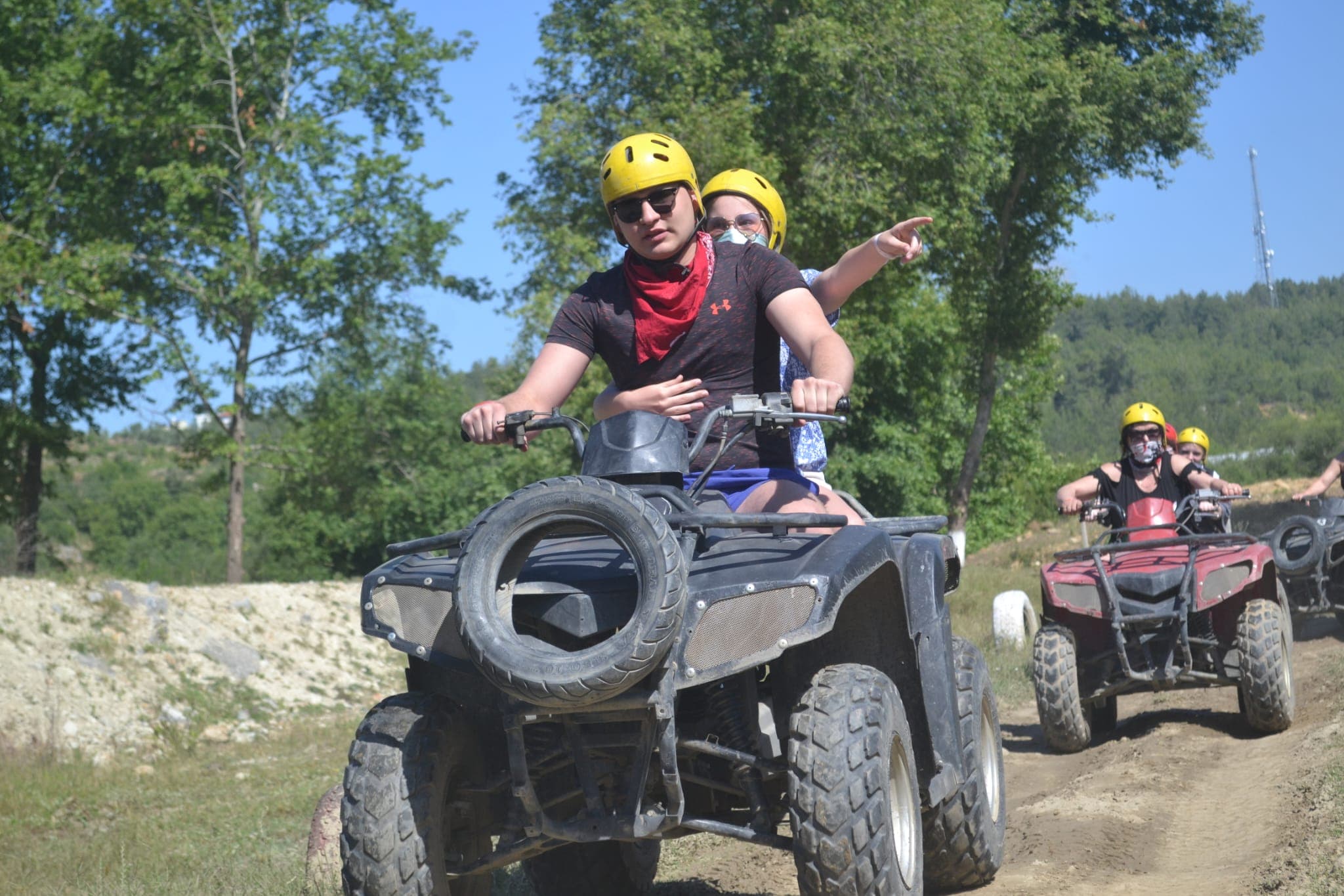 Sarı kasklı iki kişi ATV'yle toprak parkurda ilerliyor, arkalarında konvoydaki diğer araçlar