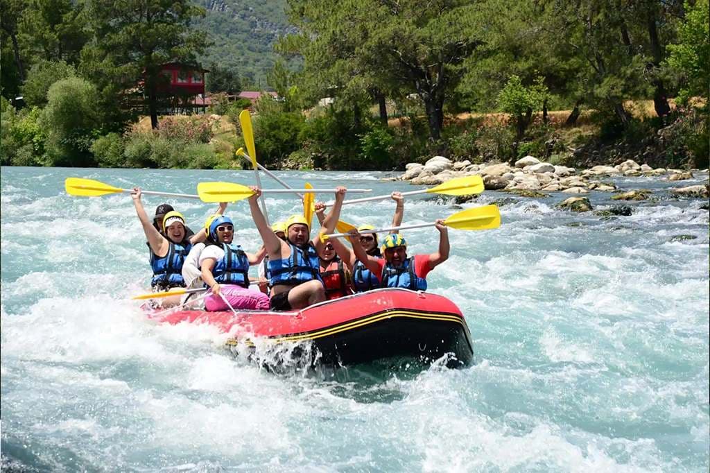 Sarı kasklı ve can yelekli bir grup kırmızı raft botunda kürekleri havaya kaldırıp Köprülü Kanyon'un beyaz sularında ilerliyor
